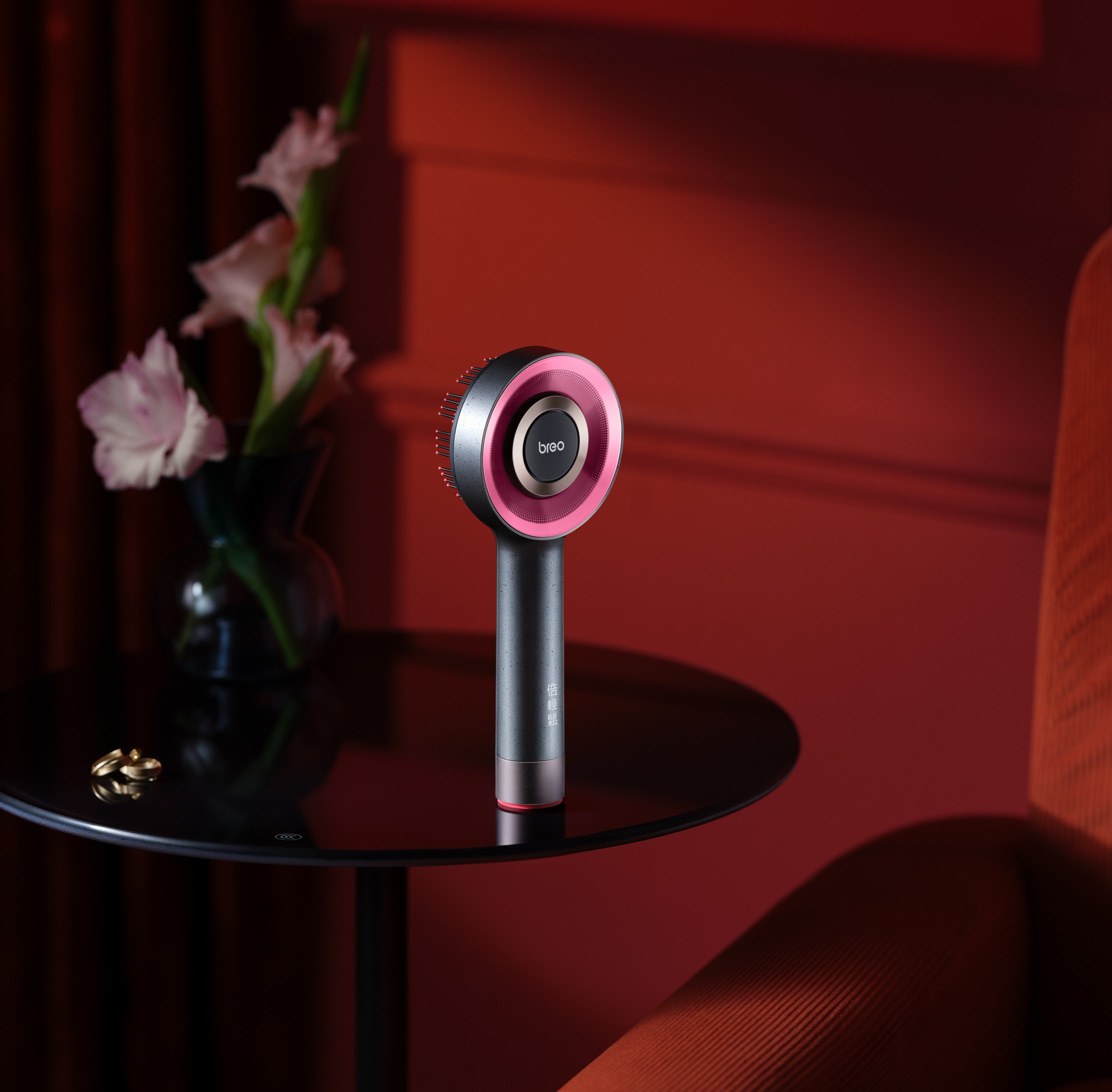 A modern Breo scalp massager placed on a table next to a vase of flowers